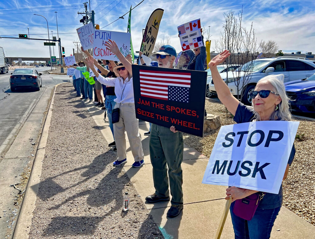 Protesters wave to a supportive motorist during Saturday's demonstration against Elon Musk's actions.