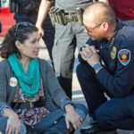 Then-Las Cruces Police Chief Jaime Montoya kneels to speak with Sarah Silva as Silva and others sit across a Las Cruces street in 2017 to protest federal immigration raids.