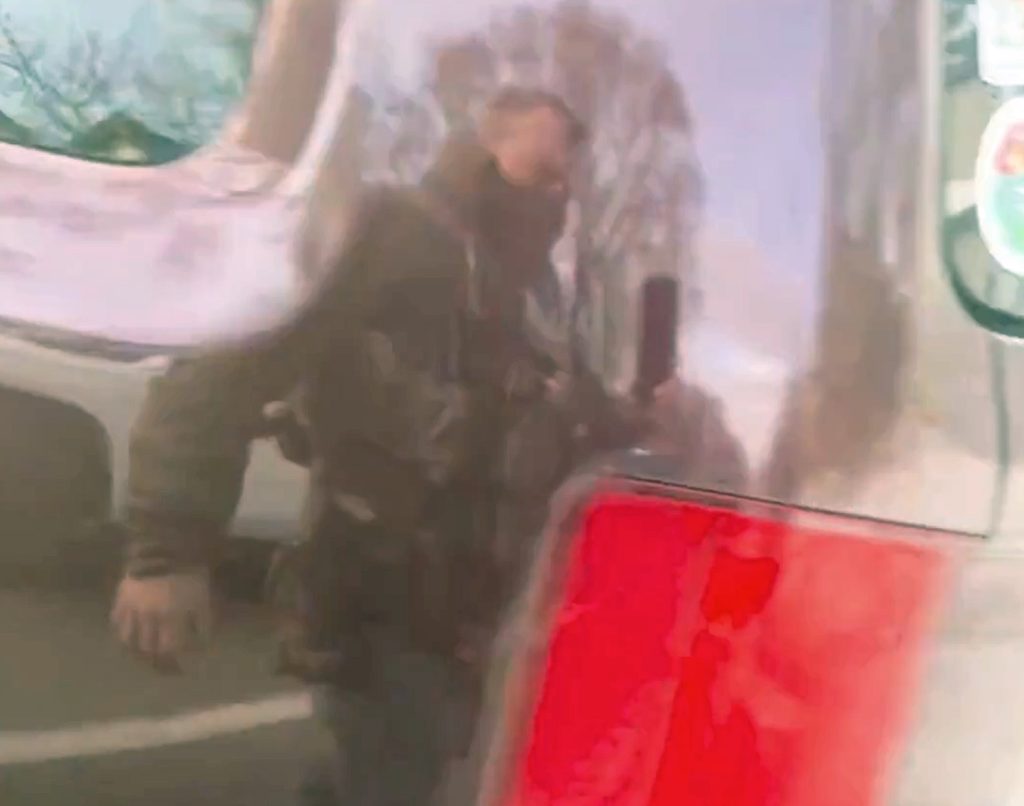 Jonathan Ross is seen in the reflection from Renee Good's vehicle while he walked around the automobile filming it. I took this image from Ross' video and edited the color a bit to make it easier to see him. Ross shot Good seconds after walking around the bumper of the vehicle.