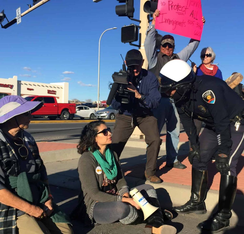 A police officer speaks with my spouse, Sarah Silva, after she and a dozen others blocked a road in Las Cruces to protest immigration raids. (Photo by Heath Haussamen)
